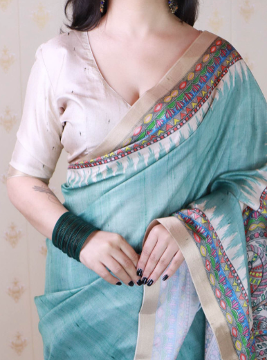 Woman wearing a turquoise saree with colorful border, holding it with one hand.