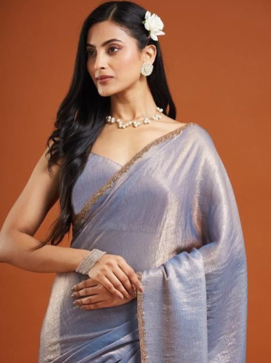 Woman wearing a light blue saree with a brown background