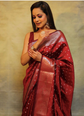 Woman wearing a red saree with intricate patterns against a beige background