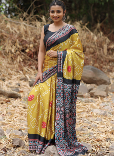 Woman wearing a yellow saree with a patterned border outdoors.