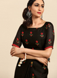 Woman wearing a black traditional outfit with red floral embroidery on a beige background