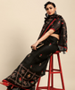 Woman wearing a black embroidered outfit sitting on a red stool against a beige background