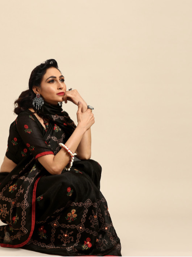 Woman wearing a black saree with red accents on a beige background
