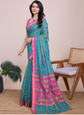 Woman wearing a teal and pink saree with a chair and plant in the background