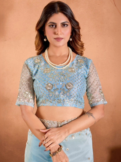 Woman wearing a light blue embroidered blouse with sheer sleeves against a brown background