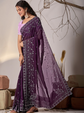 Woman wearing a purple saree with a white blouse in a minimalistic setting.
