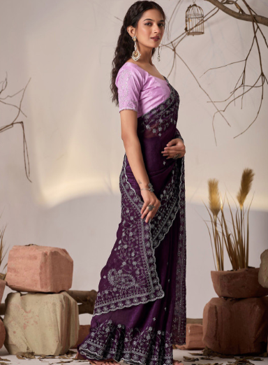 Woman wearing a purple saree with a pink blouse in a decorative setting.