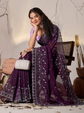 Woman wearing a purple saree with a white blouse, sitting indoors.