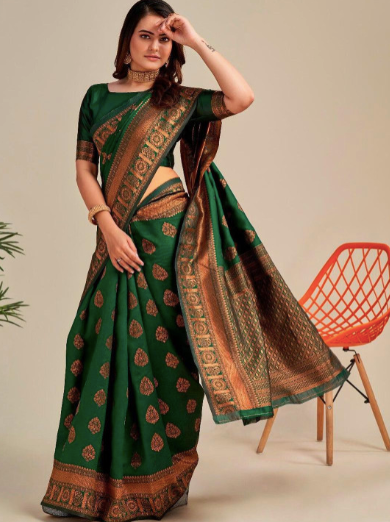 Woman wearing a green saree with brown patterns, standing next to an orange chair.