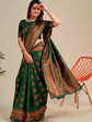 Woman wearing a green saree with brown patterns, standing next to an orange chair.