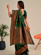 Woman wearing a green and brown saree with a plant and chair in the background