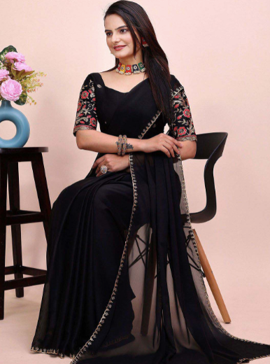 Woman in a black saree with floral blouse sitting on a chair against a pink background