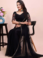 Woman in a black saree with floral blouse sitting on a chair against a pink background