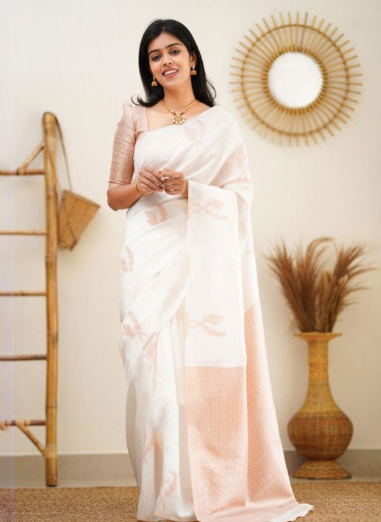 Woman in a white saree with a gold border standing in a room with decorative elements.