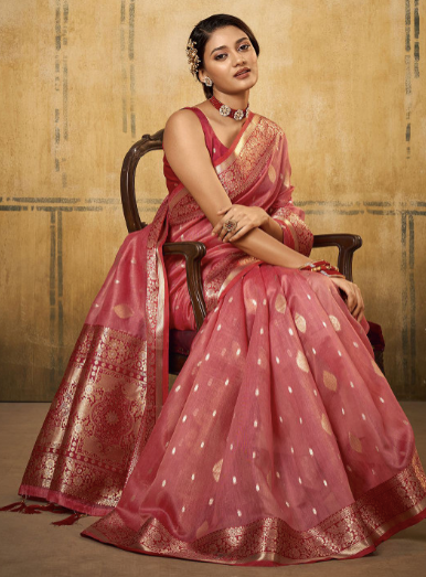 Woman in a traditional pink saree with gold patterns sitting on a chair against a beige background