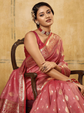 Woman in a pink saree sitting on a chair against a beige background