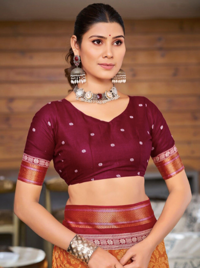 Woman wearing a traditional maroon and orange saree with jewelry against a blurred background