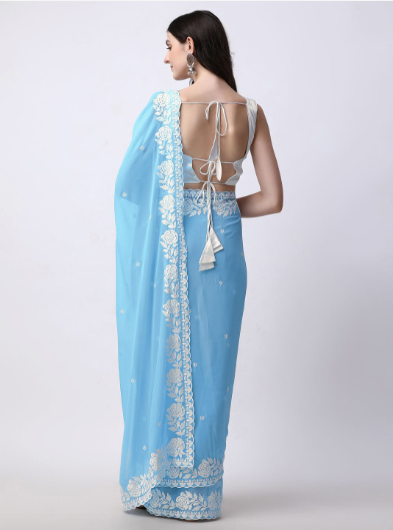 Woman wearing a light blue saree with white floral embroidery on a plain background