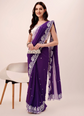 Woman wearing a purple saree with white patterns on a plain background