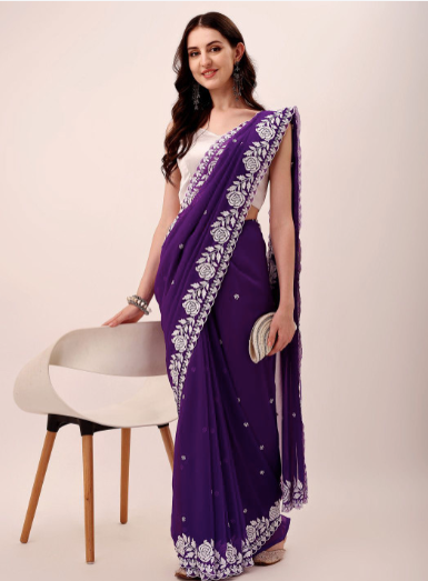 Woman wearing a purple saree with white embroidery on a plain background