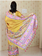 Woman wearing a yellow saree with a colorful border in a room.