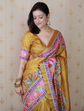 Woman wearing a yellow saree with colorful patterns against a patterned wall.