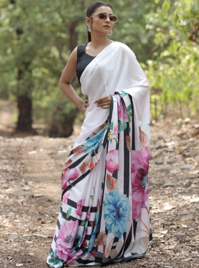 Woman wearing a white saree with colorful floral patterns outdoors.