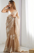Woman wearing a beige saree with white floral patterns in a minimal indoor setting.