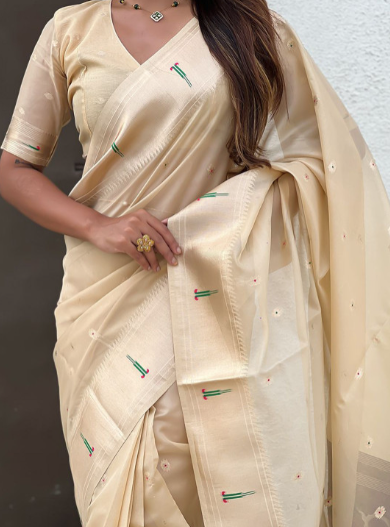 Woman wearing a beige saree with green and red patterns against a neutral background