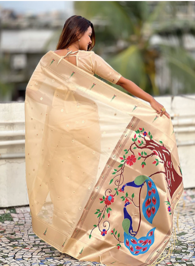 Woman wearing a beige saree with floral patterns, standing outdoors.