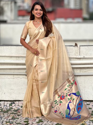 Woman wearing a beige saree with floral and peacock designs on a stone staircase.