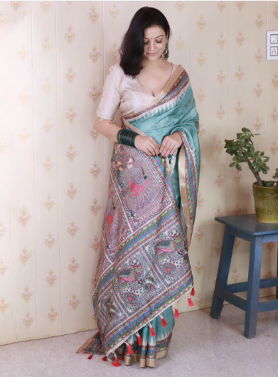 Woman wearing a colorful saree with a patterned wall and plant in the background