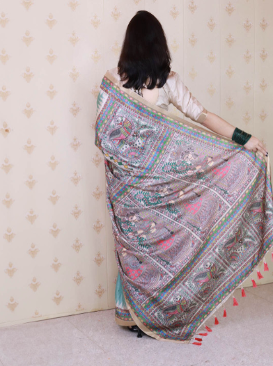 Woman holding an embroidered saree against a patterned wall.