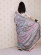 Woman holding an embroidered saree against a patterned wall.