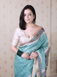 Woman wearing a light blue saree with a beige blouse against a neutral background