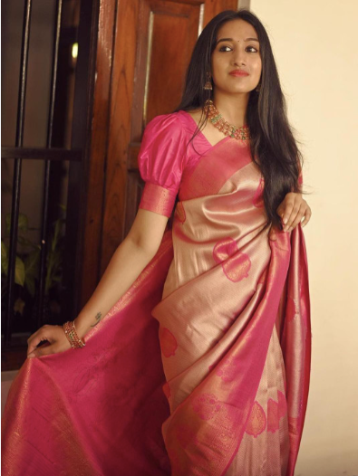 Woman wearing a pink saree with a floral pattern indoors.