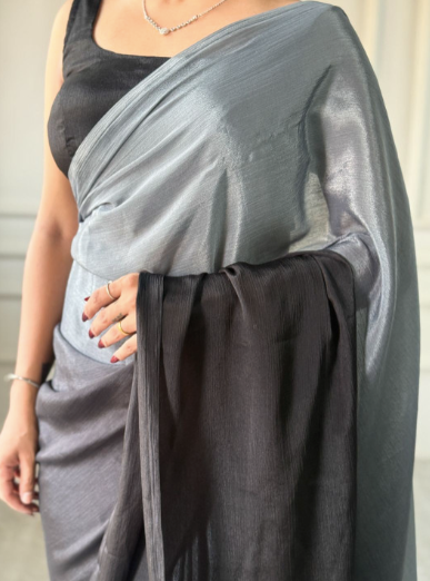Person wearing a gray draped garment over a black top against a neutral background