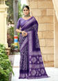 Woman wearing a purple saree with white patterns standing outdoors.