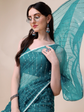 Woman wearing a teal saree with a matching blouse against a beige background