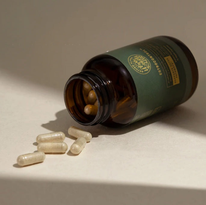 Brown glass bottle with a green label and gold emblem, containing capsules on a beige surface.
