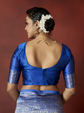 Woman wearing a blue traditional outfit with intricate designs on a red background