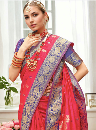 Woman wearing a traditional pink and purple saree with jewelry indoors.