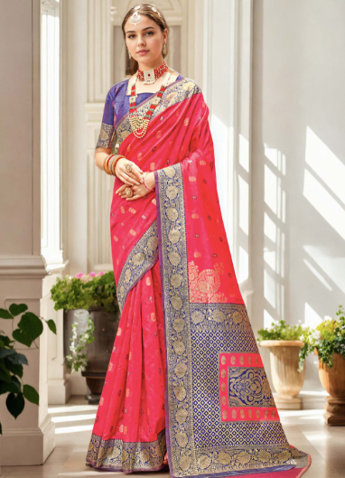 Woman wearing a vibrant red saree with gold and blue patterns in a bright room.