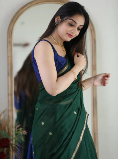 Woman in a green saree with a purple blouse adjusting her hair in front of a mirror.