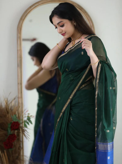 Woman adjusting a green saree in front of a mirror.