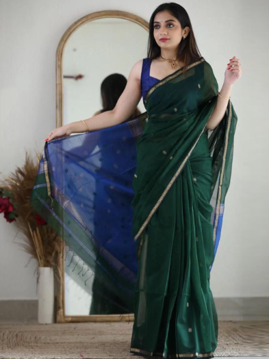 Woman in a green saree with a blue blouse standing in front of a mirror.