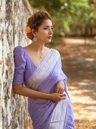 Woman in a purple saree standing against a tree with a natural background