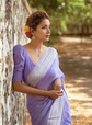 Woman in a purple saree standing against a tree with a natural background