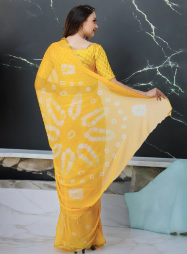 Woman wearing a yellow saree with a white pattern against a black marble wall.
