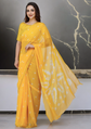 Woman wearing a yellow saree with white patterns against a marble background